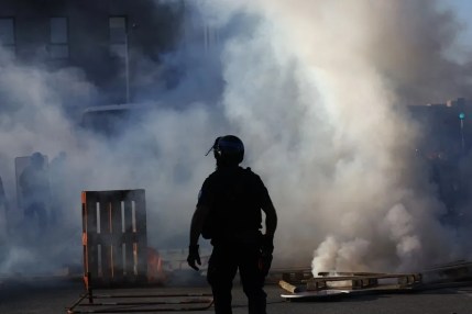 Un agente de policía camina mientras los manifestantes queman palés de madera