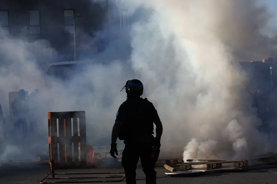 Un agente de policía camina mientras los manifestantes queman palés de madera
