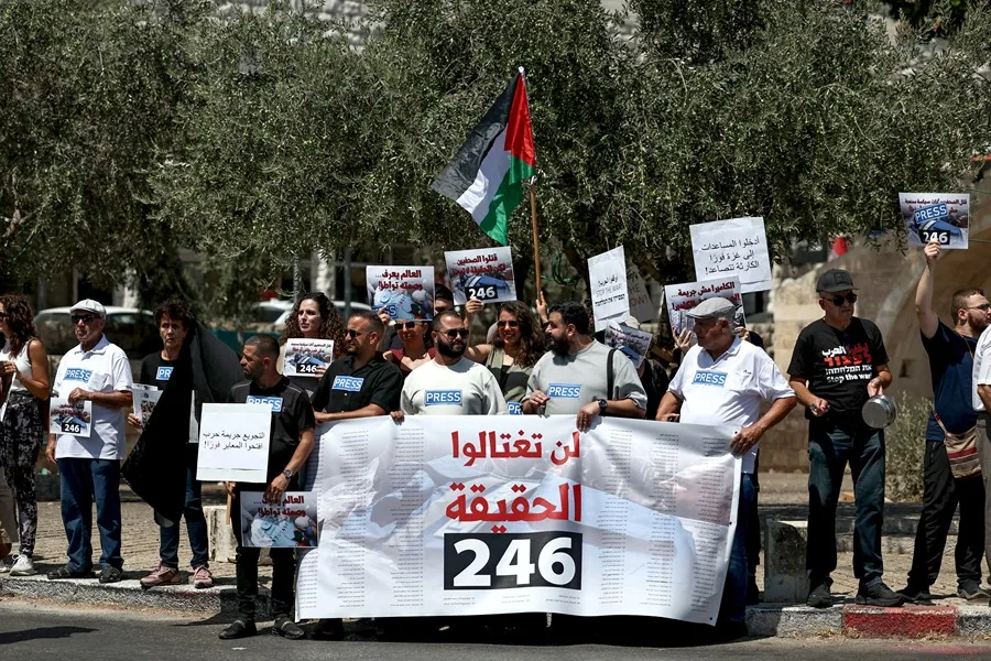 Los periodistas árabes israelíes sostienen pancartas y ondean una bandera palestina mientras se manifiestan contra los ataques a periodistas palestinos 