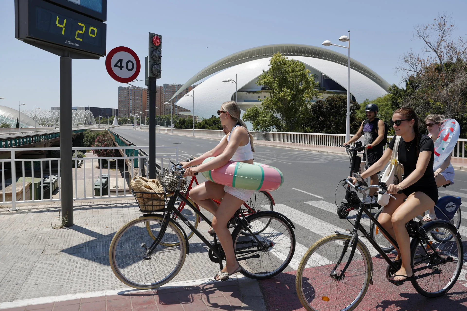 Varias jóvenes en bici al paso de un termómetro que marca 42 grados en un día del pasado mes de julio en València. EFE/Manuel Bruque