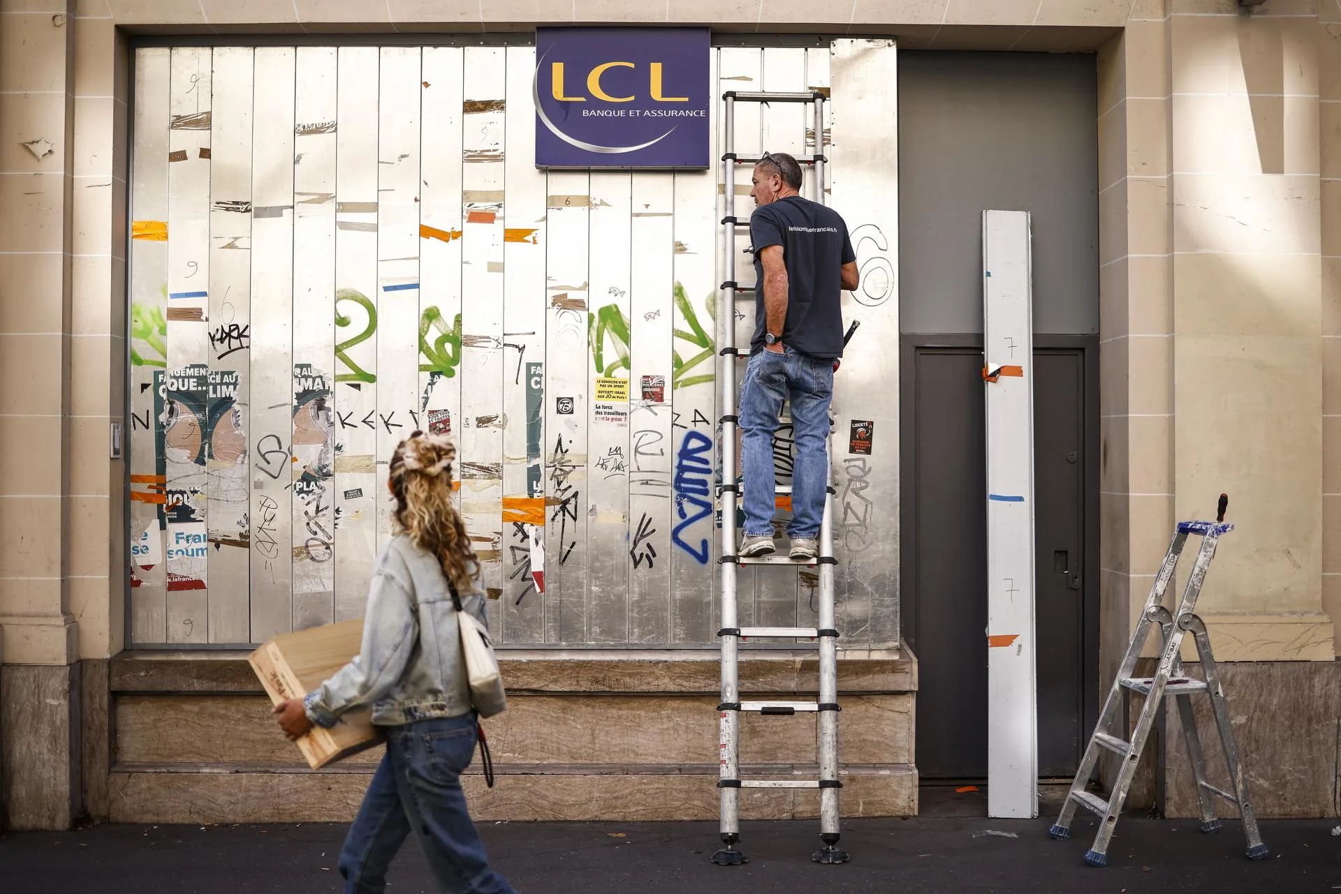 Un trabajador instala protecciones en la fachada de un banco un día antes de la huelga en París, Francia. EFE/YOAN VALAT