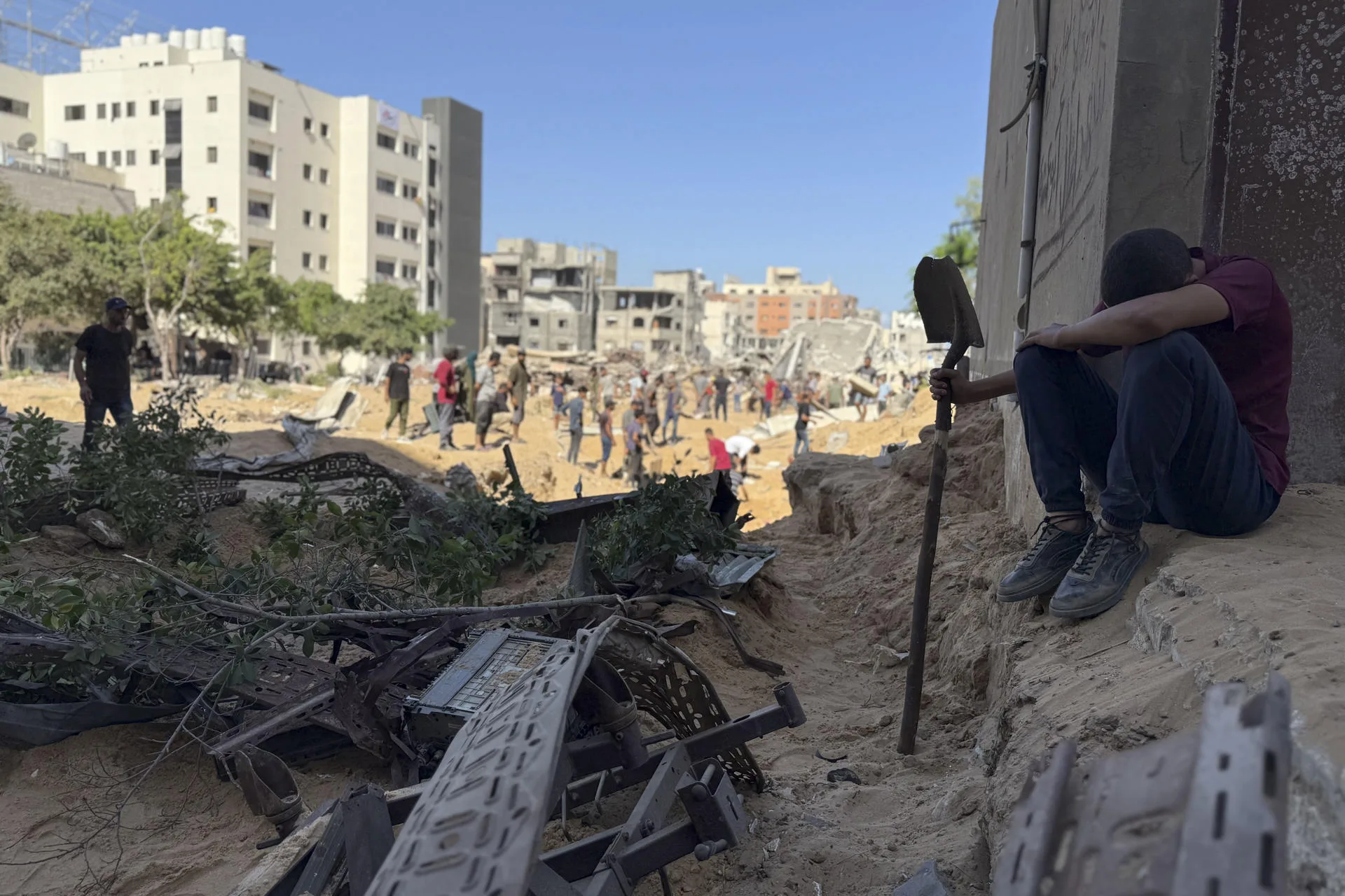 GAZA (GAZA Y CISJORDANIA), 21/09/2025.- En una fosa común improvisada detrás del Hospital Shifa, en la ciudad de Gaza, decenas de familias entierran a sus seres queridos este domingo, mientras la operación terrestre de Israel se expande, temerosos de que buscar un lugar de entierro digno les ponga en riesgo. Los cuerpos, envueltos en telas blancas, son depositados en un hoyo abierto en la arena. A su alrededor, edificios derrumbados y el zumbido constante de drones conforman el escenario de un duelo sin pausa. EFE/ Ahmad Awad
