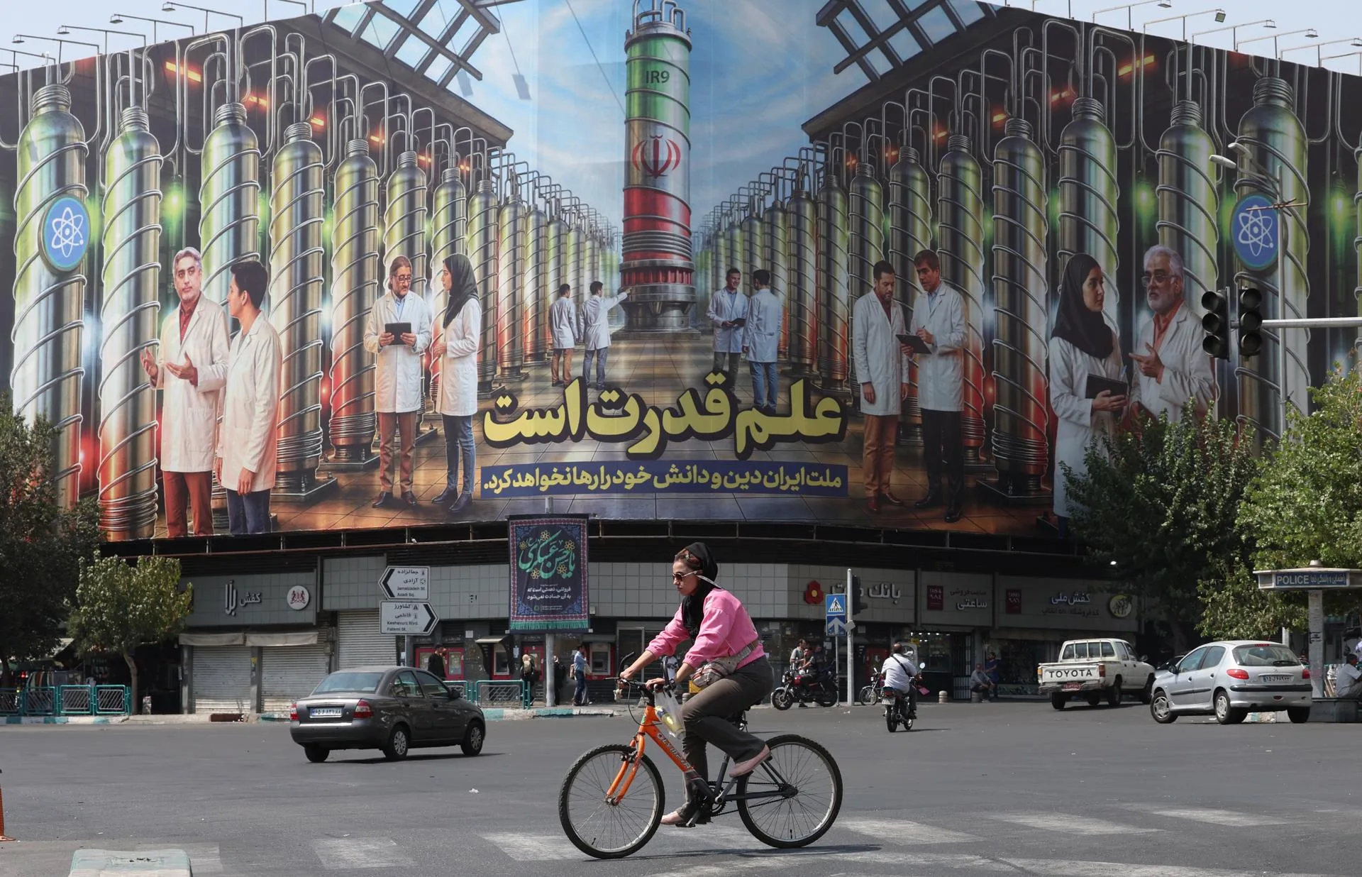 (FILE) - An Iranian woman rides a bicycle next to a billboard displaying a picture of nuclear centrifuges and a sentence reading in Persian 'Science is the power, and the Iranian nation will not abandon its religion and knowledge' at the Enghelab square in Tehran, Iran, Sep. 1, 2025. EFE/EPA/ABEDIN TAHERKENAREH