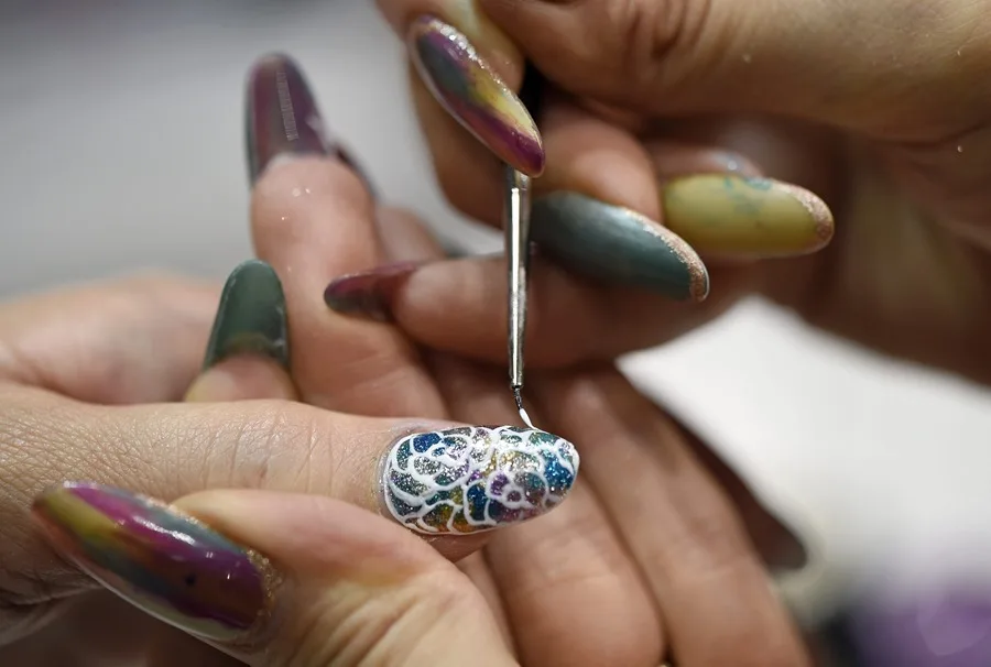 Una esteticién decora las uñas de una mujer.