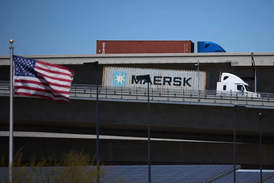 Fotografía de archivo de una bandera estadounidense ondeando al viento mientras camiones transportan contenedores de carga en Long Beach, California, EE.UU. EFE/EPA/ALLISON DINNER